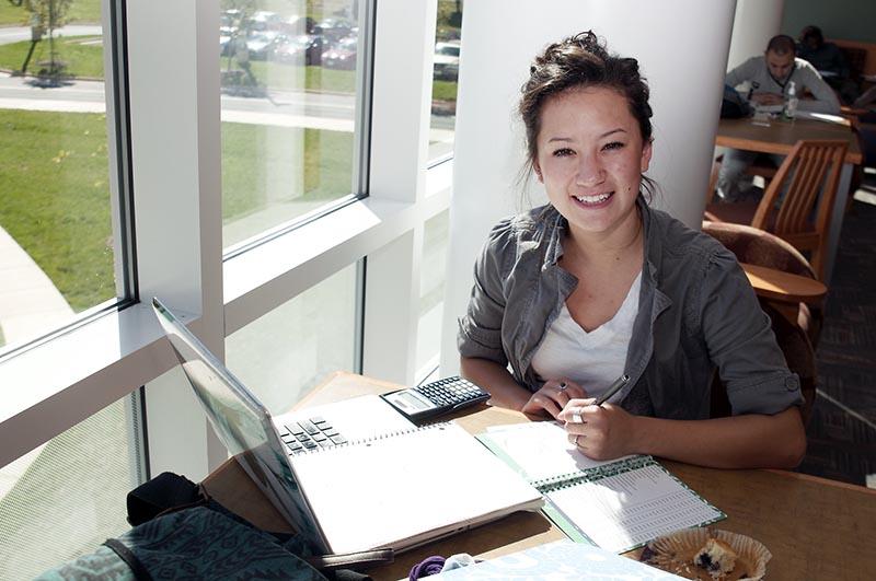 A student sitting at a table with her laptop and notebook, smiling.